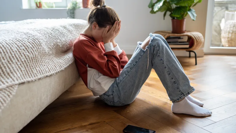 Unglückliche Teenagerin sitzt auf dem Boden in einem Raum