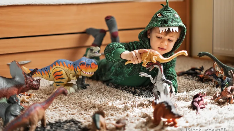 Junge im Dinokostüm spielt mit Dinofiguren